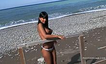 En fånig tonårsbrunett med stora falska bröst poserar på stranden